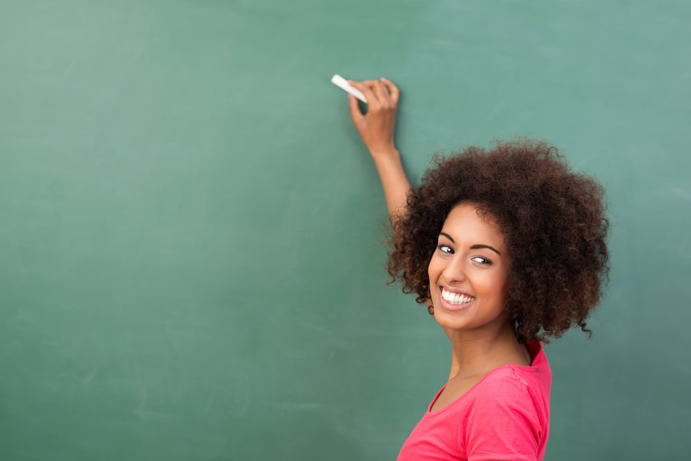 Beautiful African American student or teacher standing in front of the blank class blackboard with a piece of chalk in her hand ready to commence writing Beautiful African American student or teacher standing in front of the blank class blackboard with a piece of chalk in her hand ready to commence writing