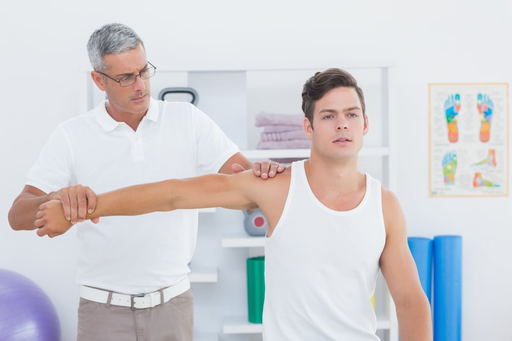 Doctor stretching a young man arm in medical office