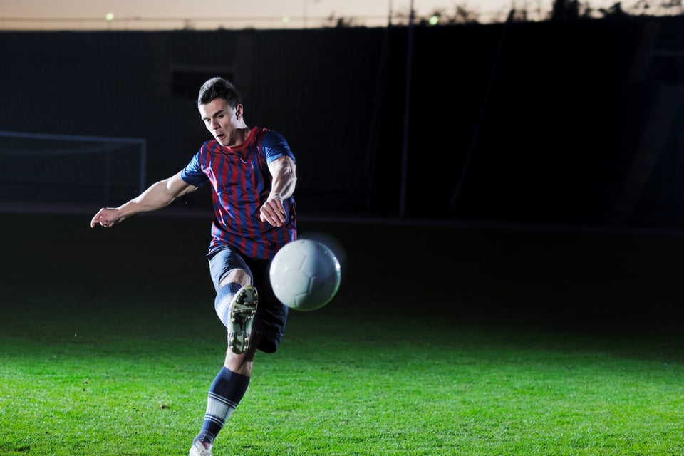 soccer player doing kick with ball on football stadium field isolated on black background in night